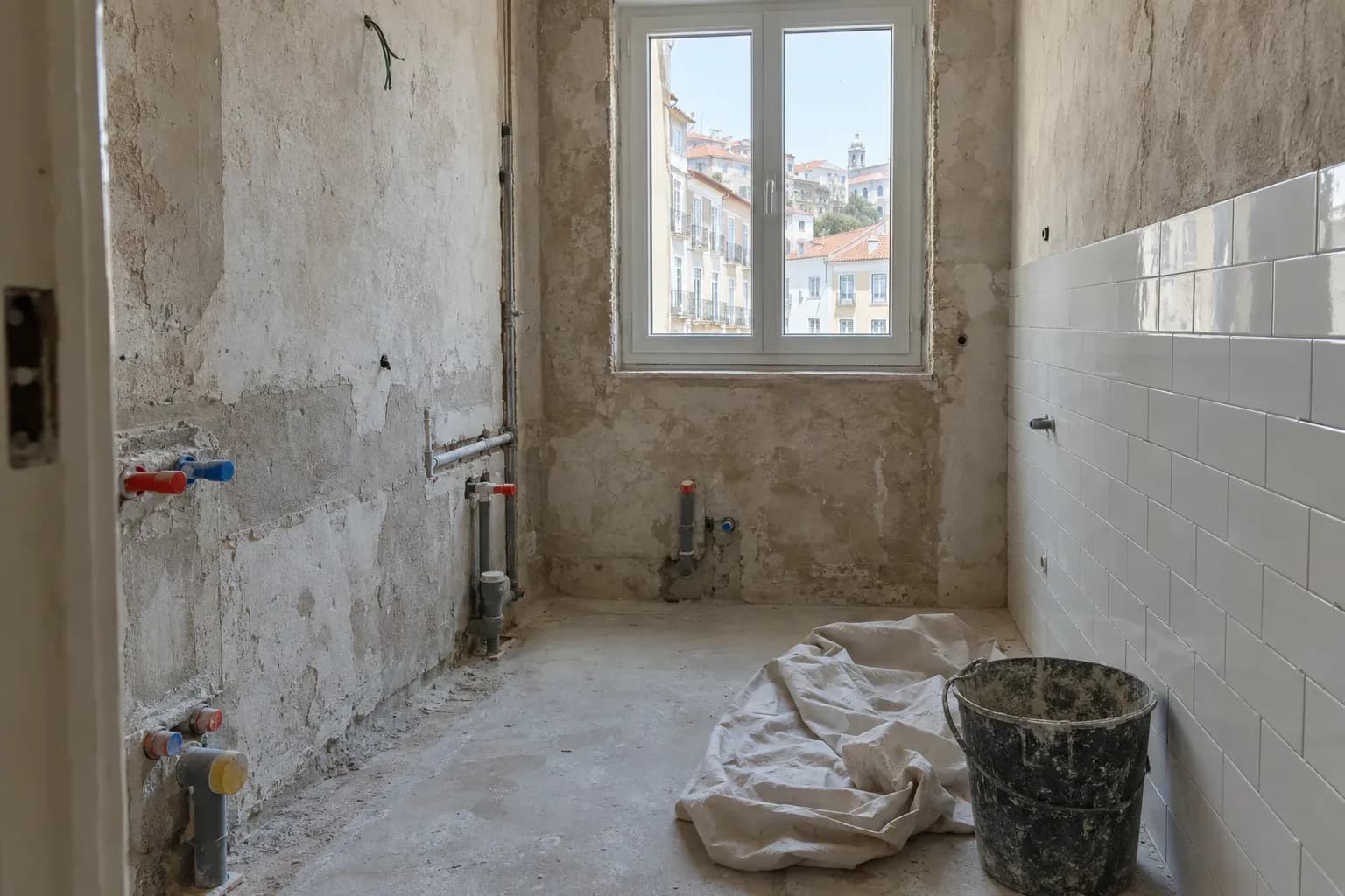 Casa de banho em obras, com reboco nas paredes, canos por montar e um lençol no chão